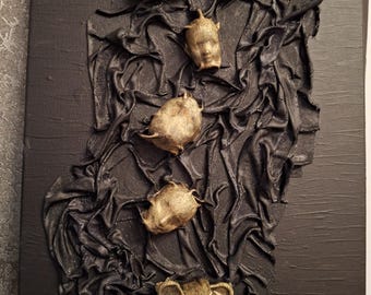 May include: A rectangular black canvas featuring a central vertical strip of heavily textured, draped black fabric. Five small, gold-colored, three-dimensional sculpted heads are arranged in a column along the center of the fabric.
