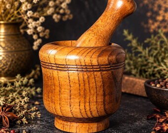 May include: A polished wooden mortar and pestle set featuring a natural light brown wood grain finish. The mortar has a cylindrical body with a wide, rounded rim and a stable base, while the pestle is smooth, tapered, and rounded at the top.