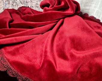 May include: A deep red velvet fabric draped in soft folds, featuring a matching intricate scalloped lace trim along the edges. The material has a smooth, plush texture that catches the light, creating subtle variations in the rich crimson color.