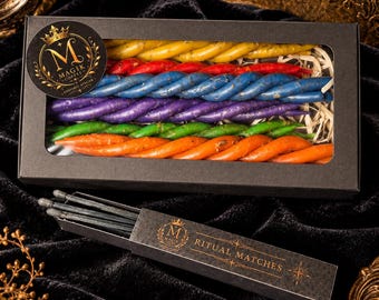 May include: A black rectangular box containing rows of twisted candles in yellow, red, blue, purple, green, and orange. A circular sticker on the box features a crown and the text Magik Coffee. A separate black box labeled Ritual Matches contains dark matches.