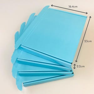 May include: A stack of unfolded light blue cardboard boxes. Each box measures 16.4 cm wide, 23 cm long, and 2.2 cm high. The boxes are arranged in a fan-like pattern, showcasing their folded edges and overall shape.