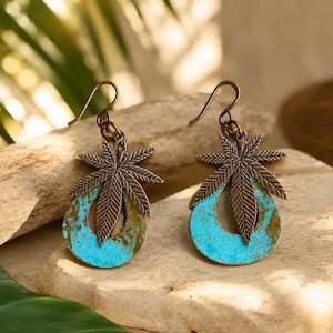 May include: A pair of dangle earrings featuring a bronze-toned metal leaf charm attached to a teardrop-shaped pendant with a textured, bright turquoise patina finish. The earrings include curved metal ear wires for secure attachment.