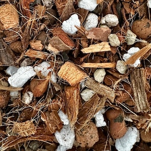 Peut inclure: Gros plan d'un mélange de composants de terreau organique. L'image montre un mélange de fibres de coco brunes, de copeaux de bois, de perlite blanche et de petits galets de couleur claire. La texture est grossière et naturelle, adaptée à la croissance des plantes.