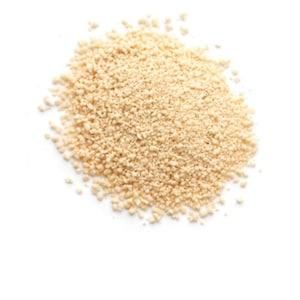 May include: A pile of light tan, granular material against a white background. The texture appears coarse and slightly uneven, with small, irregular particles. The overall shape is a loose, rounded cluster, suggesting a dry, powdery substance.