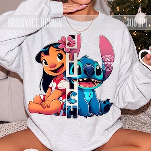 Puede incluir: Una sudadera gris claro de cuello redondo con un estampado gráfico de Lilo y Stitch. Una banda vertical blanca con el texto negro STITCH separa a los personajes. Lilo lleva un vestido rojo con flores y Stitch es de color azul.