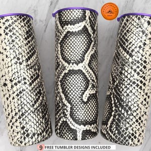 May include: Three cylindrical tumblers featuring a black and white snakeskin pattern. Each tumbler is topped with a solid purple lid. A small circular orange logo with a mountain graphic is visible, and text at the bottom reads 9 FREE TUMBLER DESIGNS INCLUDED.
