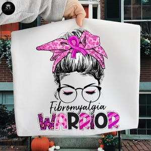 May include: White fabric with a graphic of a woman with glasses, a pink ribbon, and a pink patterned headscarf. The text "Fibromyalgia WARRIOR" is below the image. The word "WARRIOR" is in a pink leopard print.