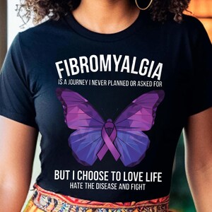 Puede incluir: Camiseta negra con la palabra "FIBROMYALGIA" sobre un dise&ntilde;o de mariposa morada. El texto debajo de la mariposa dice: "PERO ELIJO AMAR LA VIDA, ODIAR LA ENFERMEDAD Y LUCHAR".
