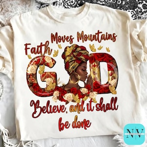 Peut inclure: T-shirt crème avec un graphisme représentant les mots "Faith Moves Mountains" et "Believe, and it shall be done." Le mot "GOD" est stylisé avec des roses et une femme portant un foulard. Des créoles dorées sont visibles.