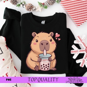 May include: Black sweatshirt featuring a cartoon capybara drinking bubble tea. The capybara is light brown with pink cheeks and is holding a cup with a straw. The words "TOP QUALITY" are printed on the bottom of the image.