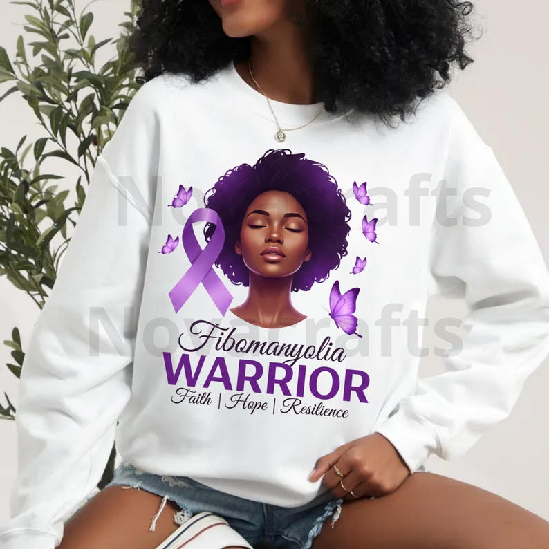 Puede incluir: Sudadera blanca con lazo morado, mariposas y retrato de mujer. El texto dice "Guerrera de Fibromialgia" con "Fe | Esperanza | Resiliencia". El dise&ntilde;o utiliza tonos morados.