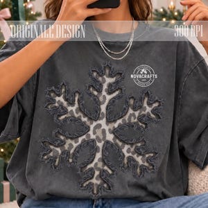 Pode incluir: Uma t-shirt cinzento-carvão com um grande gráfico central de floco de neve com padrão de leopardo e bordas desfiadas. O texto ORIGINALE DESIGN e 300 DPI aparece no topo, com um logótipo circular NOVACRAFTS 2025 à direita.
