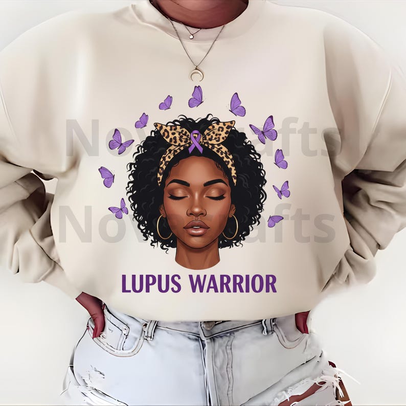 Puede incluir: Sudadera color crema con un gr&aacute;fico de una mujer con los ojos cerrados, adornada con una diadema con estampado de leopardo y mariposas moradas. El texto "LUPUS WARRIOR" est&aacute; impreso en morado. La mujer tiene aros dorados.
