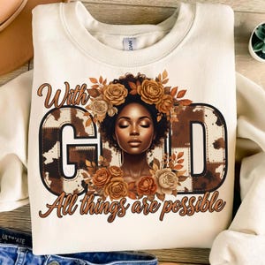 Peut inclure: Sweat-shirt crème avec l'inscription "With God All things are possible". Le mot "GOD" est orné d'un motif imitation peau de vache marron. Une femme aux yeux fermés et une couronne florale se trouve au centre du mot "GOD".