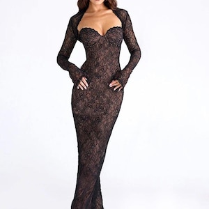 May include: A black lace dress with a sweetheart neckline and long sleeves. The dress is floor-length and form-fitting, with a matching bolero jacket. The intricate lace pattern covers the entire dress, creating a delicate and elegant look.