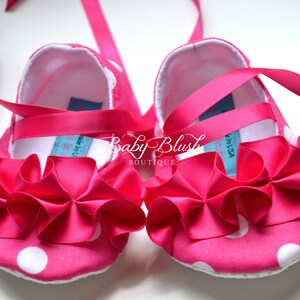 May include: Pink baby shoes with white polka dots and a pink satin bow. The shoes have a white lining and a pink ribbon tie.