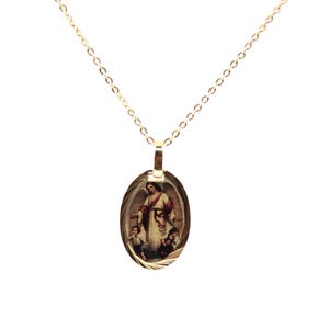 May include: A gold-toned oval pendant necklace featuring a detailed religious illustration of a guardian angel standing behind two children. The pendant hangs from a delicate gold-coloured chain with small, uniform circular links.