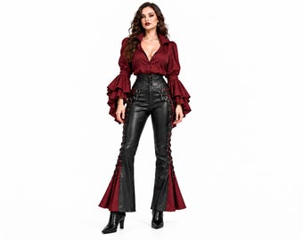 Könnte beinhalten: Eine dunkelrote Langarmbluse mit gestuften Glockenärmeln und Knopfleiste, kombiniert mit einer schwarzen High-Waist-Hose mit seitlicher Schnürung, Metallringen und ausgestellten Beinabschlüssen mit roten Stoffeinsätzen.