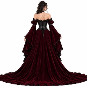 Back view of a Gothic Victorian gown showing the black leather corset back with lace-up ties, off-shoulder burgundy velvet sleeves, and a long flowing burgundy velvet train with black ruffles.
