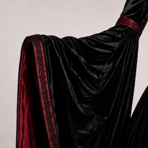 Close-up of a dramatic bell sleeve showing gathered velvet fabric, burgundy lining, decorative trim, seams and natural folds.