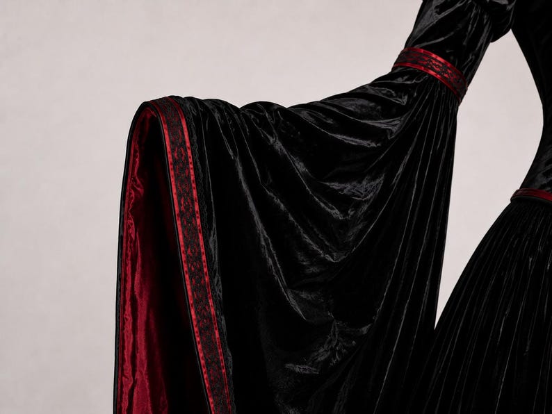 Close-up of a dramatic bell sleeve showing gathered velvet fabric, burgundy lining, decorative trim, seams and natural folds.