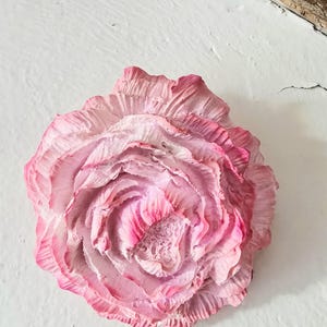 Peut inclure: Gros plan sur une fleur en papier rose aux détails complexes. Les couches de la fleur présentent un dégradé de rose, du clair au foncé. Les pétales ont un aspect texturé et froissé. La fleur est montée sur une surface blanche.