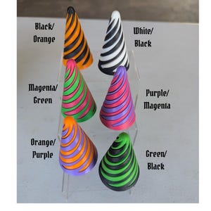 May include: A collection of six cone-shaped decorative objects in various color combinations. The cones are striped with colors like black and orange, white and black, magenta and green, purple and magenta, orange and purple, and green and black. Text on the image indicates the color combinations.