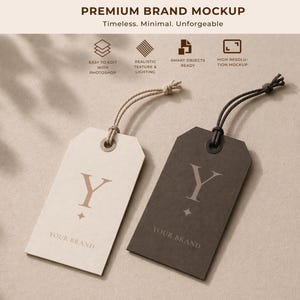 Pode incluir: Duas etiquetas retangulares com cordas. Uma é branco-sujo, a outra é cinza escuro. Ambas as etiquetas têm a letra "Y" e um design de estrela. O texto "YOUR BRAND" está impresso na parte inferior. O texto "PREMIUM BRAND MOCKUP" está no topo.
