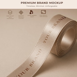 May include: A roll of beige satin ribbon with the words "YOUR BRAND" printed in a darker tone. The ribbon is unrolled, revealing the text. The image also includes text that reads "PREMIUM BRAND MOCKUP" and other text.