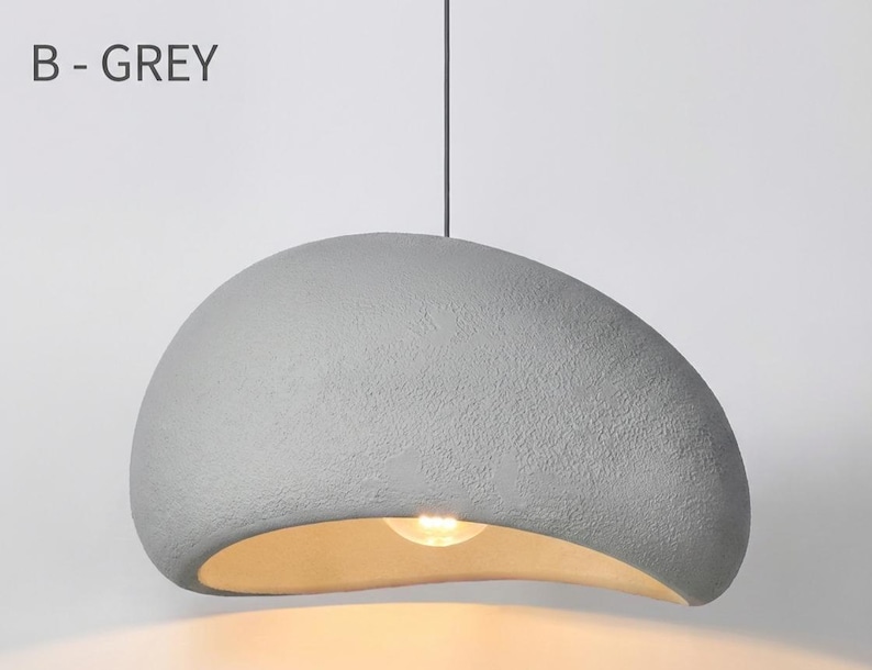 May include: A grey, textured pendant light with a curved, organic shape. The light fixture has a warm, golden interior and hangs from a single cord. The text "B - GREY" is visible in the upper left corner.