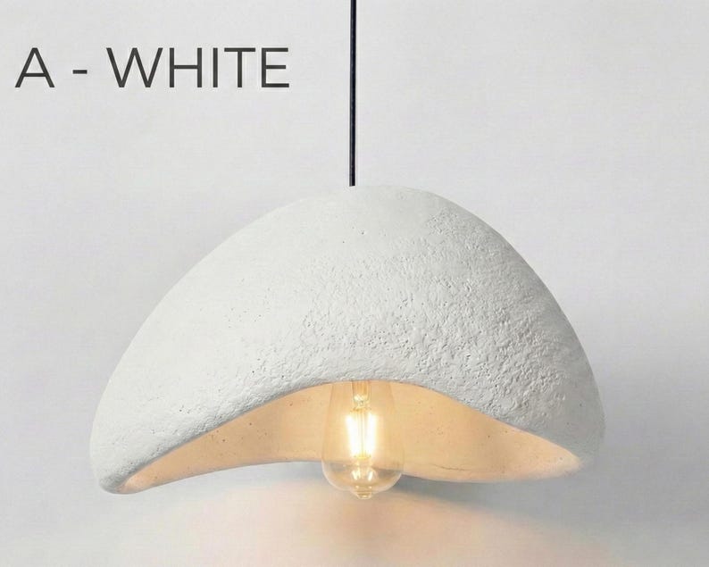 May include: White, textured pendant light fixture with a unique, organic shape. The light has a bulb visible at the bottom and is suspended from a black cord. The text "A - WHITE" is above the light.