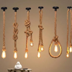 May include: A collection of rustic pendant lights with exposed Edison bulbs. The lights are suspended from the ceiling by thick, textured rope, with various knot designs. The bulbs emit a warm, inviting glow, perfect for a vintage or industrial aesthetic.
