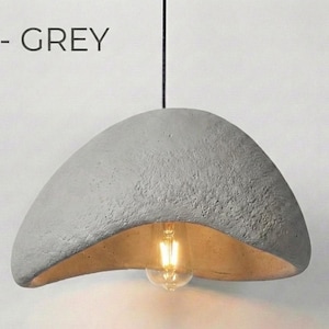 May include: A grey, textured, pendant light fixture with a curved, bowl-like shade. The interior of the shade is a warm, golden color, and a light bulb is visible. The text "A - GREY" is above the light.