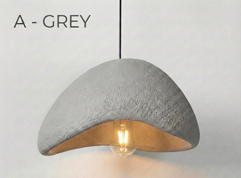 May include: A grey, textured, pendant light fixture with a curved, bowl-like shade. The interior of the shade is a warm, golden color, and a light bulb is visible. The text "A - GREY" is above the light.