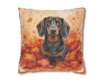 May include: A decorative square pillow featuring a watercolor illustration of a black and tan dachshund dog sitting in a pile of orange and red autumn leaves. The pillow has an orange border and a cream-colored background.