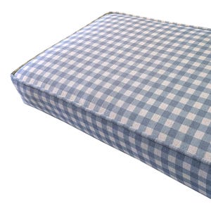May include: A rectangular cushion with a blue and white gingham pattern. The cushion has a thick, padded design with a light blue border. The fabric is tightly woven, creating a classic, country-style aesthetic.