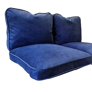 May include: Two-piece navy blue velvet sofa cushions. Each cushion has a square shape with a rounded top and a contrasting dark blue piping around the edges. The cushions are designed for comfort and style.