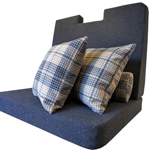 May include: A dark blue upholstered bench with a back and two plaid pillows. The pillows feature a blue, white, and tan plaid pattern. The bench is a solid dark blue color and has a modern design.