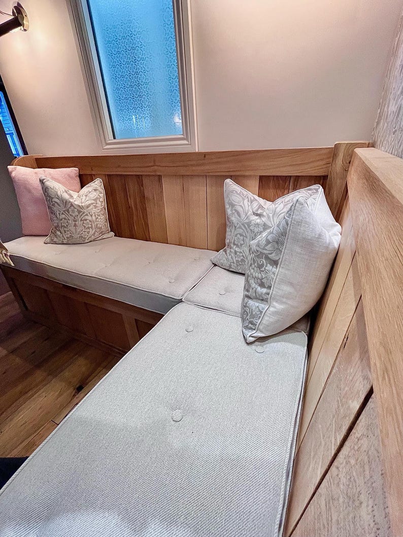 A kitchen dining banquette seating area with a set of made to measure foam bench cushions. The storage seating area is made up with light brown wood panelling and it has three piped and buttoned bench seating cushions on top made with an oatmeal, cream coloured fabric. The hardwearing twill fabric bench cushion cover has a stain resistant treatment making this box edged bench cushion perfect for use around kids, children and pets. Hardwearing and easy clean seat cushions for benches and seats.