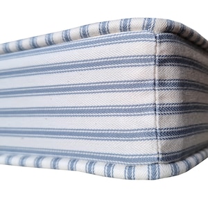 May include: Close-up of a rectangular cushion with a blue and white striped pattern. The fabric has a textured appearance, with the stripes running horizontally across the surface. The edges are neatly finished with a matching blue and white trim.