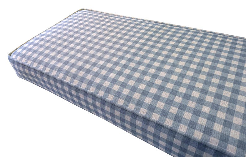 A plump, custom made indoor bench cushion with green gingham cotton and linne upholstery fabric cover. A foam and dacron wadding seat cushion for a dining room bench seat with piping cord at the edges. The bench cushion cover has a blue and off white check pattern in a hard wearing fabric. Stain resistant cover for a storage bench cushion with a zip at the back for cleaning. Made to measure upholstery foam cushion for a wooden seating bench. Window seat cushion in gingham pattern fabric.