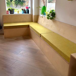 A bright kitchen banquette seating area build in wooden storage cupboard lift up lid seat. Wooden flooring kitchen. Yellow indoor bench cushions made to fit the plywood seating bench. Thick firm foam supportive home office seating cushions made to measure. Clean, unpiped bench cushions wipe clean, machine washable bench cushion covers, pet friendly. Bespoke high quality long lasting bench cushion kept in place with anti-slip cloth non permanent fixing. Welt free box edge seat bad & back cushion