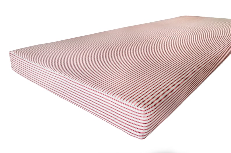A large, thick day bed cushion made with firm upholstery foam inside. The cushion is 10cm thick and is supportive and comfortable to sit on. The bench cushion has a cover with a zip at the back. The cover is made with a red and white french style ticking stripe fabric which is 100% cotton. The bench cushion is plain with no piping giving a sleek, contemporary aesthetic. The cushion can have an additional stain resistant treatment making it perfect for use around children or kids in dining spaces