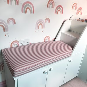 A custom shape seat cushion for a built in bed in a child's room. The cushion has firm foam with dacron on inside and looks plush and comfortable. One end of the small bench cushion has two cut out shapes giving a perfect fit around the small ladder leading up to a bunk bed. The cushion has been well made with a pink and off white stripes fabric which is stain resistant. The cushion has piped edges adding strength to the seams and the cover has a zip at the back.