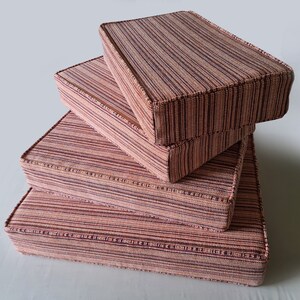 May include: A stack of four square cushions with a striped pattern in shades of pink and brown. The cushions are made of a woven fabric and have a subtle texture.