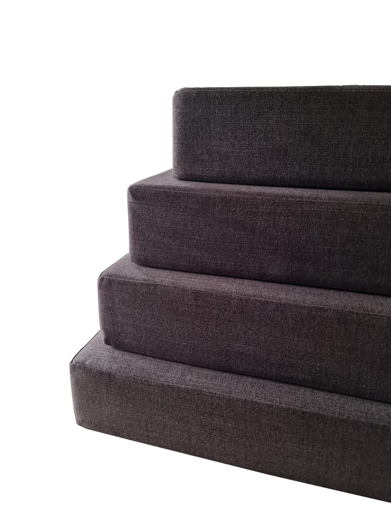 Camper van conversion bed cushions in a dark grey easy care fabric. Performance fabric bench cushion covers for stowaway bed in camper van renovation. Thick, hard wearing, durable firm foam inners. Fire safe. Eco friendly latex option for sleeping on. Cotton, wipe clean, pet friendly van mattress cushions. Shaped around van wall. Bulkhead cushions. Made in the UK by a small family company. Luxury motor home cushion replacement. Sprinter stowaway bed. VW platform bed camper van cushions.