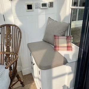 A small dining room window seat storage cupboard with a firm foam bench cushion on top to add extra seating for the room. The shaped bench cushion has a curve at one corner which is a perfect fit. The quality bench cushion has a 100% cotton cover made in a french style ticking fabric in a blue and beige colour. The ticking fabric is made in the UK by a small local company. The Bench cushion is made by a very small family company based in Yorkshire near Halifax.
