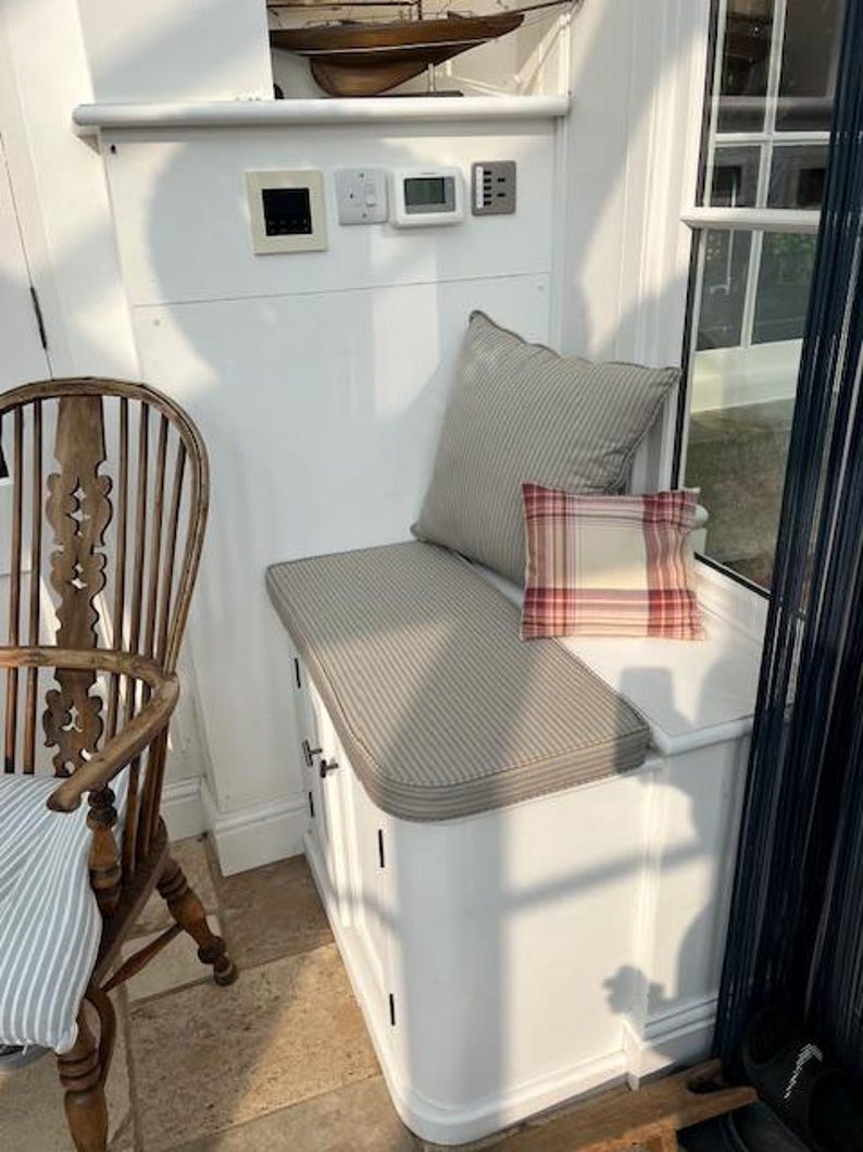 A small dining room window seat storage cupboard with a firm foam bench cushion on top to add extra seating for the room. The shaped bench cushion has a curve at one corner which is a perfect fit. The quality bench cushion has a 100% cotton cover made in a french style ticking fabric in a blue and beige colour. The ticking fabric is made in the UK by a small local company. The Bench cushion is made by a very small family company based in Yorkshire near Halifax.