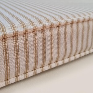 100% cotton ticking fabric bench cushion cover in off white and beige stripes. Made to measure bench cushion with firm seating foam and dacron wrap for comfortable seat cushions. Bench cushion in french style ticking fabric. Striped bench cushion in cream and neutral coloured stripe fabric. Made in the UK bench cushions with zippers, piping and button tufting. Hand made window seat cushions, any shape or size, cut outs, curves, odd shapes. Foam seat cushions made for church pew seats in stripes