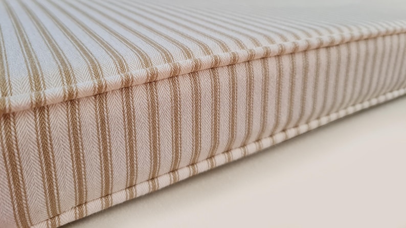 100% cotton ticking fabric bench cushion cover in off white and beige stripes. Made to measure bench cushion with firm seating foam and dacron wrap for comfortable seat cushions. Bench cushion in french style ticking fabric. Striped bench cushion in cream and neutral coloured stripe fabric. Made in the UK bench cushions with zippers, piping and button tufting. Hand made window seat cushions, any shape or size, cut outs, curves, odd shapes. Foam seat cushions made for church pew seats in stripes